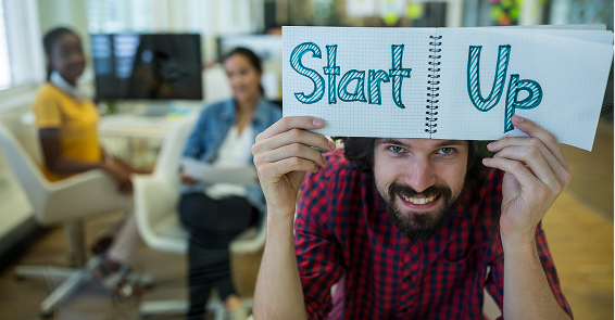 Enthusiastic entrepreneur holding a 'Start Up' notebook in a modern office environment